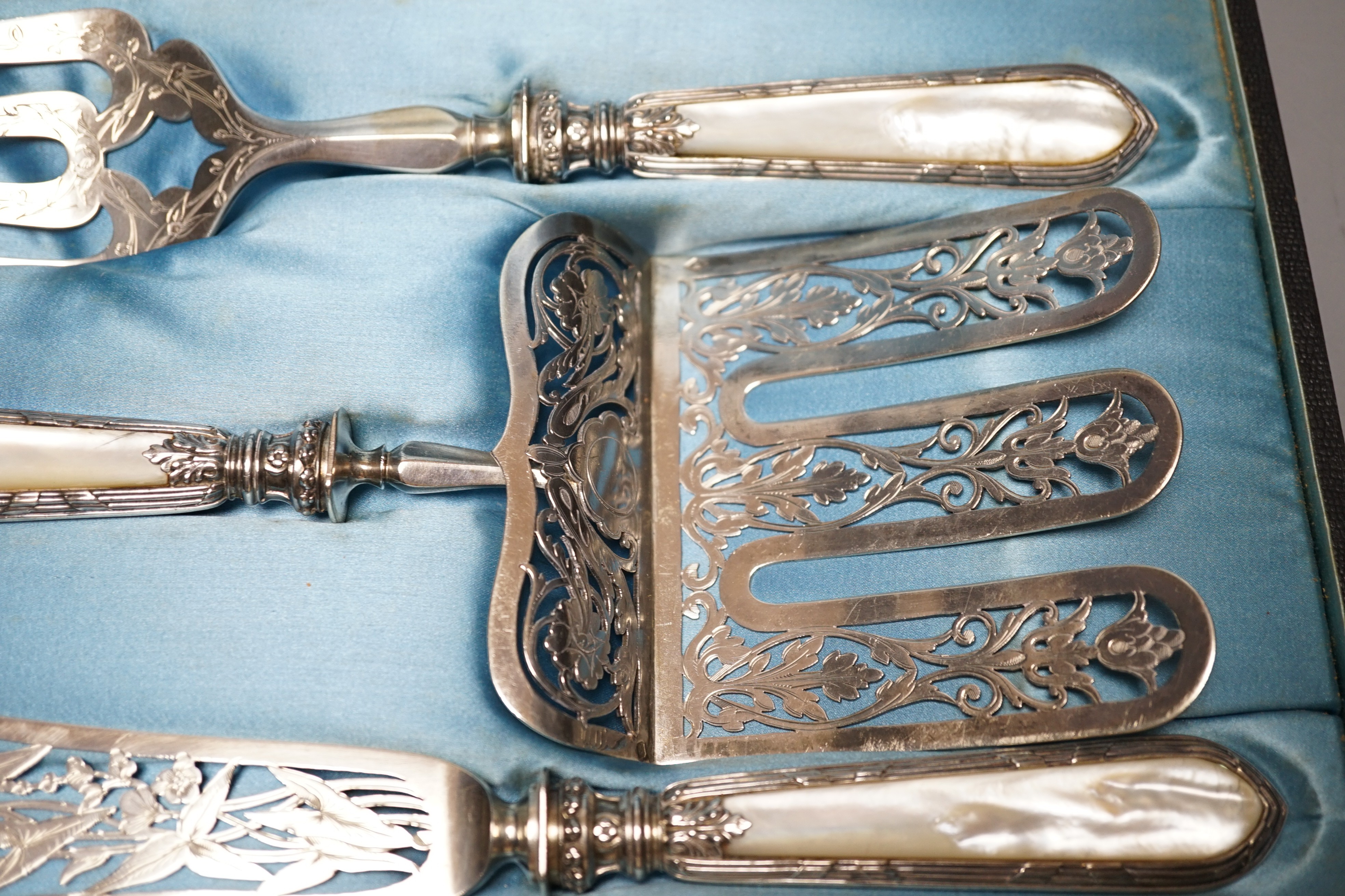 A cased ornate French white metal and mother of pearl mounted serving set, comprising a pair of fish servers and a cake server, maker JM.
